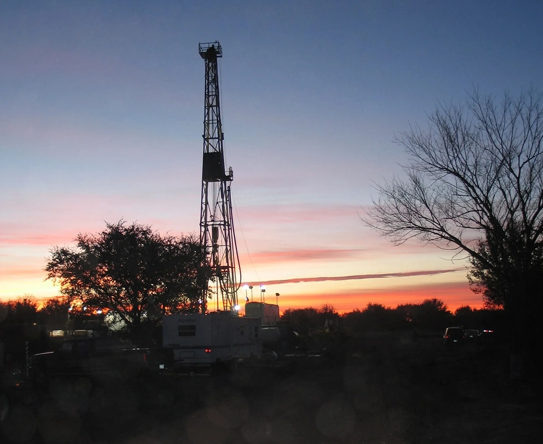 A drilling rig is seen at sunset in the distance.